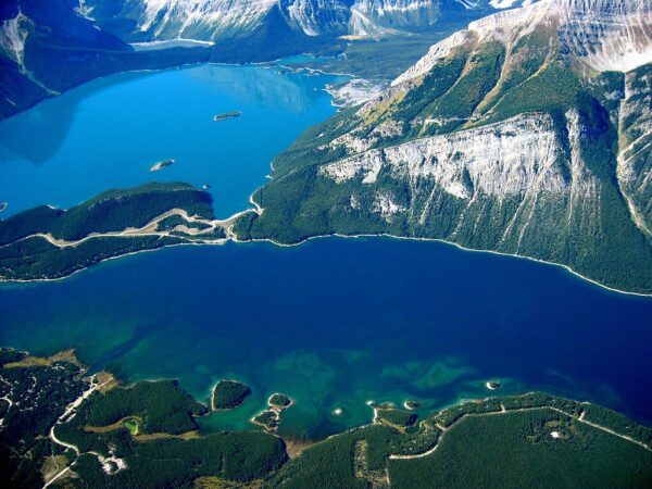 Alt Text: Aerial view of Lower Kananaskis Lake trail winding along the turquoise waters surrounded by snow-capped Rocky Mountains and forested shores in Alberta, Canada.