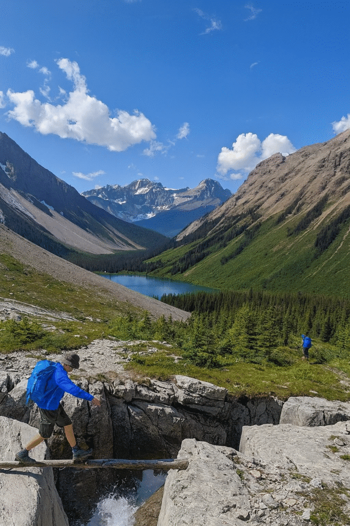 Scenic view of Turbine Canyon Hike with hikers crossing rocks, alpine lake, and rugged mountains in Alberta.