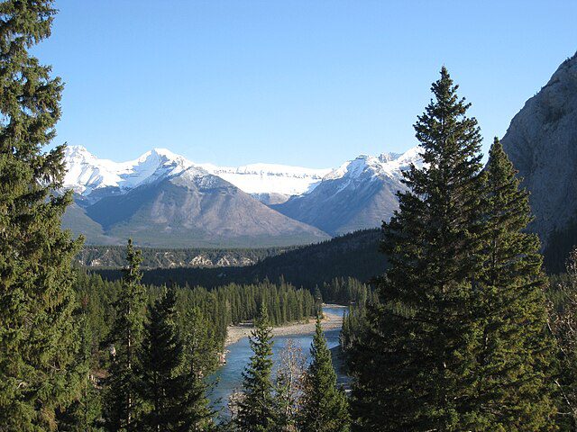 Mountain landscape view in Banff Canada in October with snow-capped peaks, evergreen forest, and river valley under clear blue sky